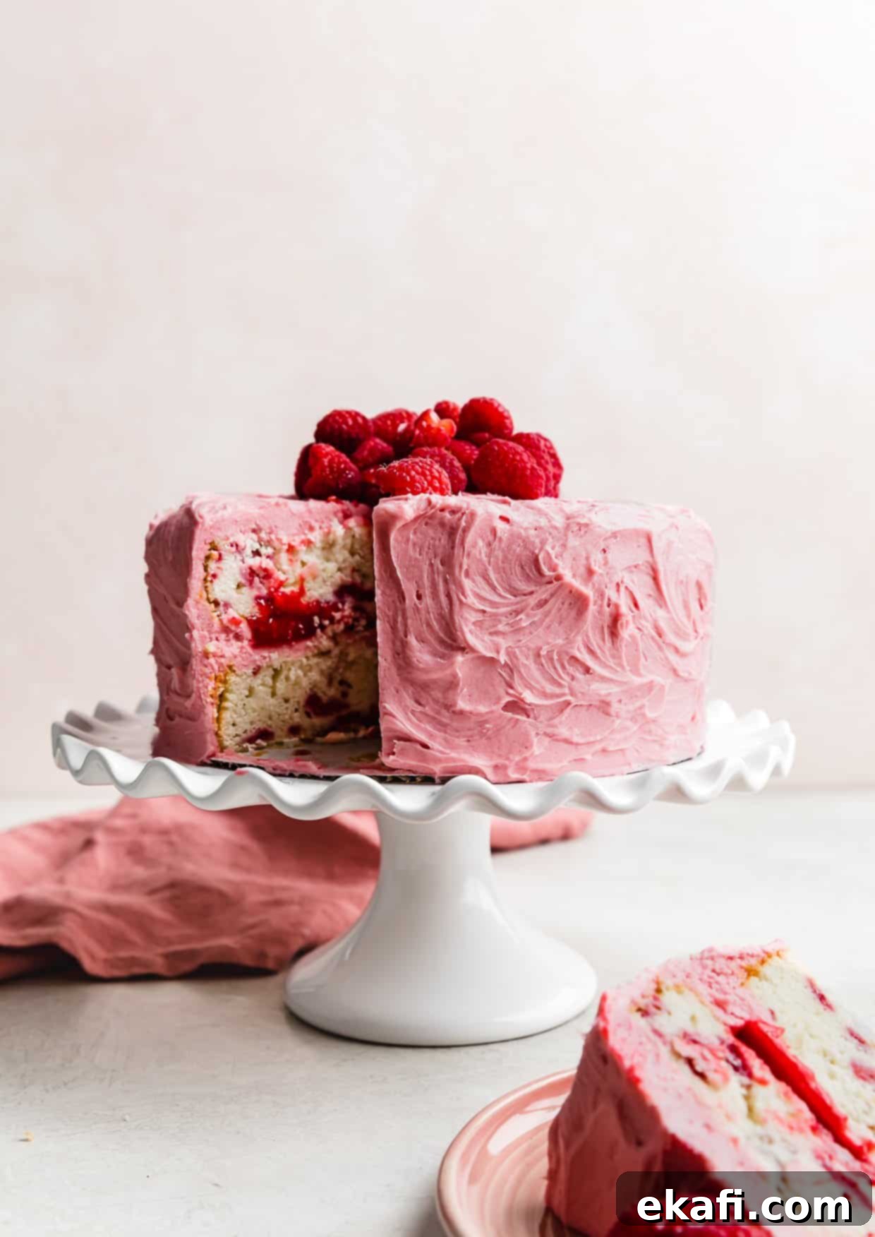 Perfect Lemon Raspberry Cake 12 A Lemon Raspberry Cake on a white cake stand with one slice of cake removed from the full cake.