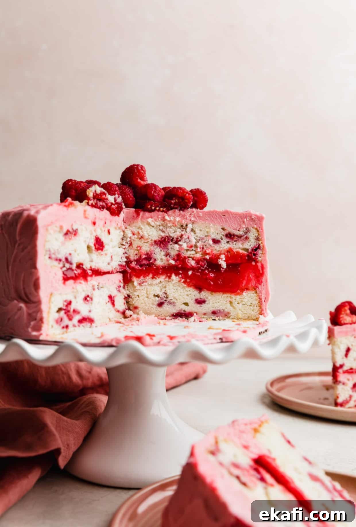 Perfect Lemon Raspberry Cake 13 A two layer Lemon Raspberry Cake on a white cake stand with a slice of cake removed showing the raspberry filling between each layer.