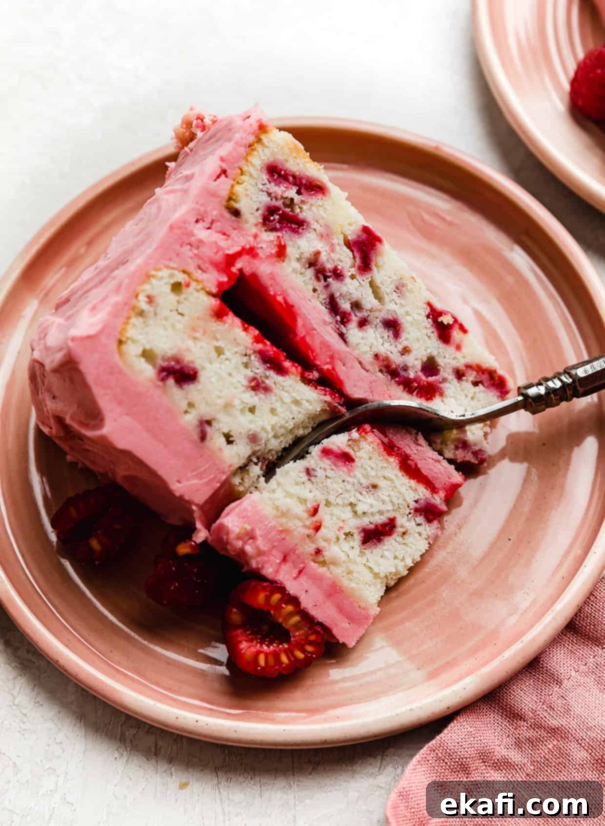 Perfect Lemon Raspberry Cake 14 A slice of Lemon Raspberry Cake that has raspberry filing between each layer, on a pink plate with a fork cutting into the cake.