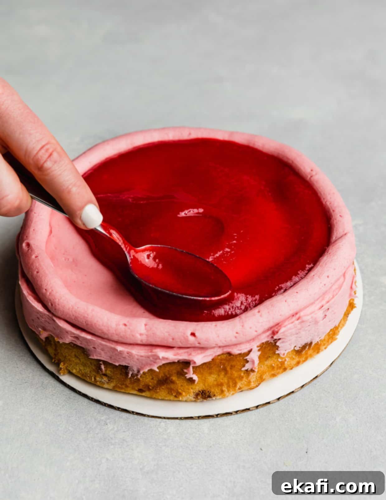 Perfect Lemon Raspberry Cake 8 A spoon spreading a raspberry filling overtop a round cake layer that has a buttercream dam piped around the perimeter.