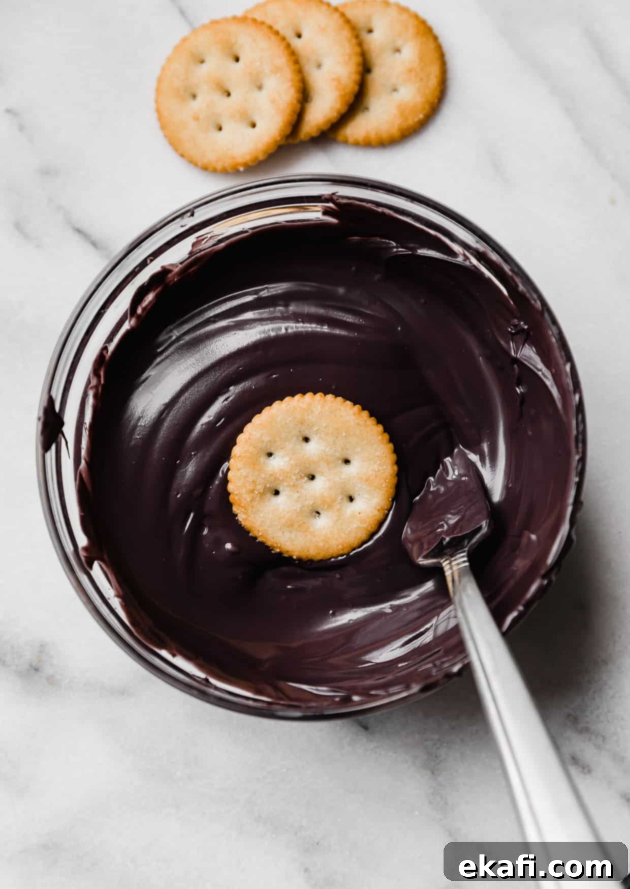 Haunted Snaps 5 A ritz cracker in a bowl filled with black melted chocolate, ready for dipping.