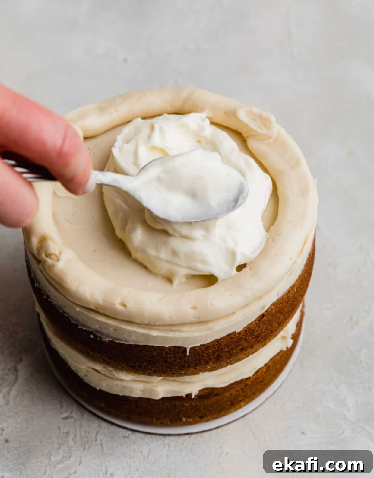 Golden Oreo Dream Cake 9 A spoon smearing a white whipped cream cheese filling overtop a Golden Oreo Cake layer.