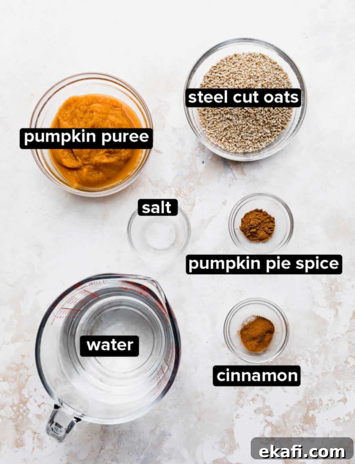 Autumn Pumpkin Spice Steel Cut Oats 3 A vibrant flat lay of Pumpkin Steel Cut Oats ingredients: a bowl of raw oats, canned pumpkin puree, cinnamon sticks, and pumpkin pie spice, all arranged beautifully on a textured white background.