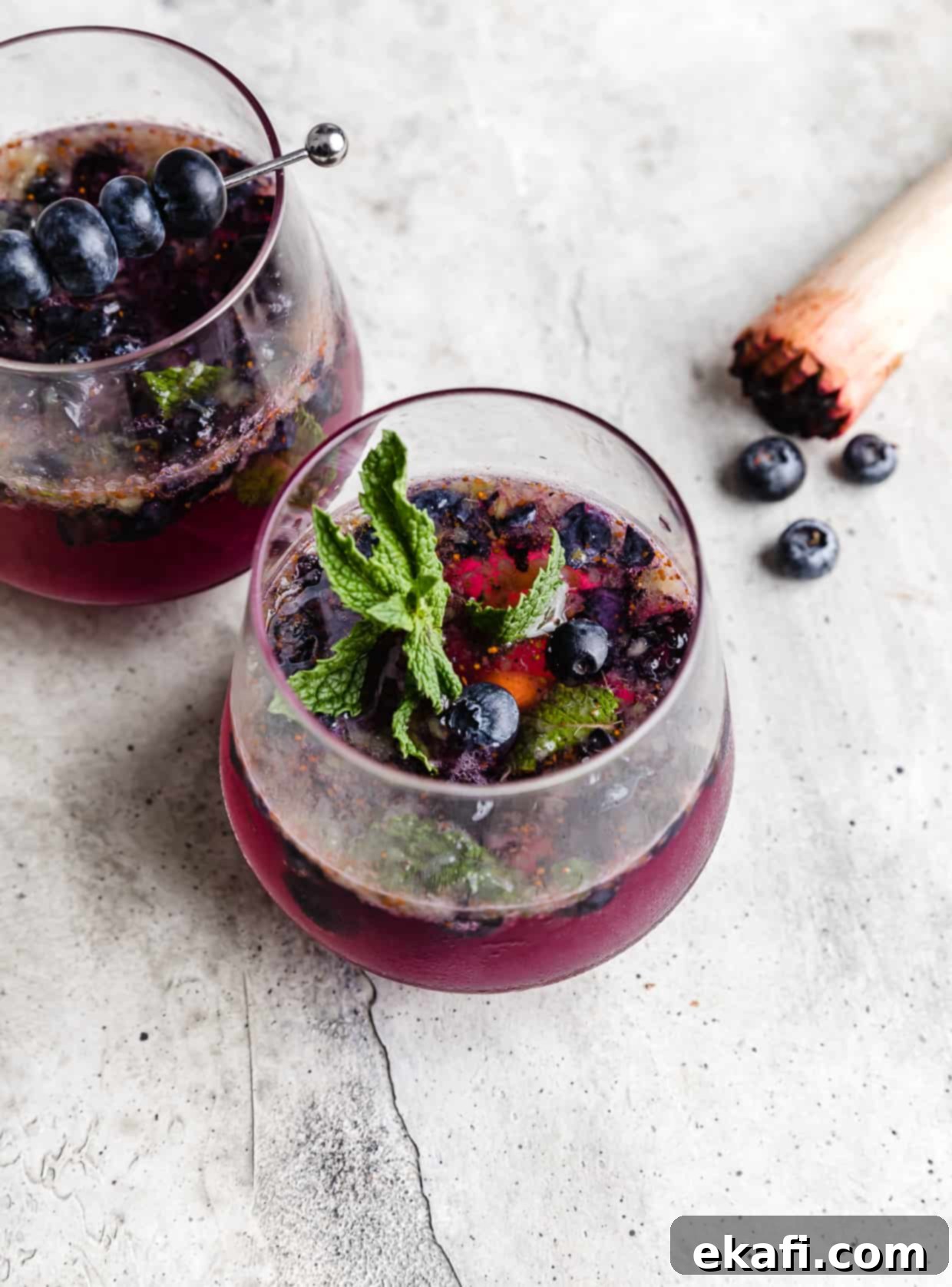 Blueberry Bliss Quencher 2 A glass filled halfway with a vibrant Blueberry Mint Mocktail, garnished with a fresh mint sprig and scattered blueberries.