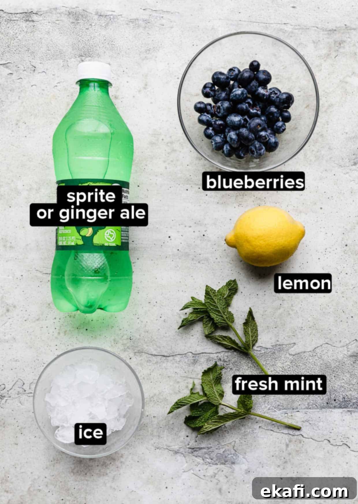 Blueberry Bliss Quencher 3 A flat lay of fresh ingredients used to make a blueberry mocktail: blueberries, mint leaves, a lemon, and a bottle of clear soda.