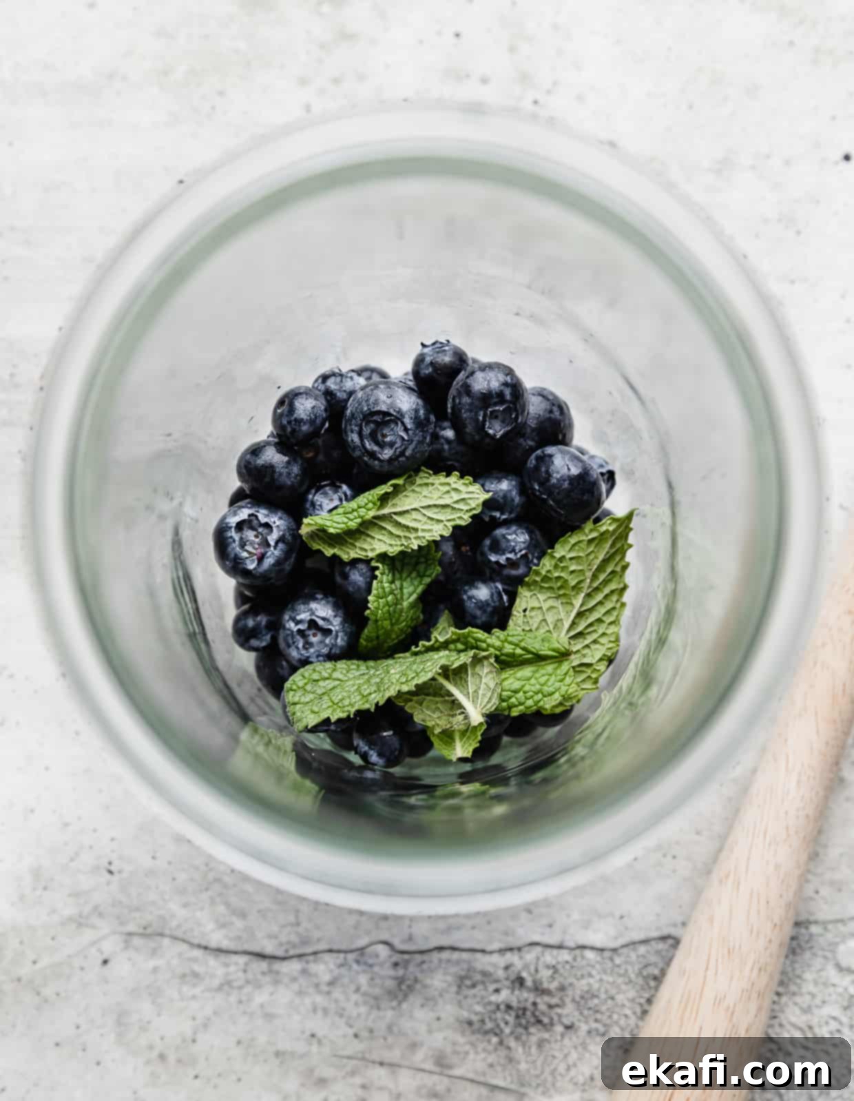 Blueberry Bliss Quencher 4 A glass jar with a handful of fresh blueberries and mint leaves at the bottom, ready for muddling to make a blueberry mocktail.