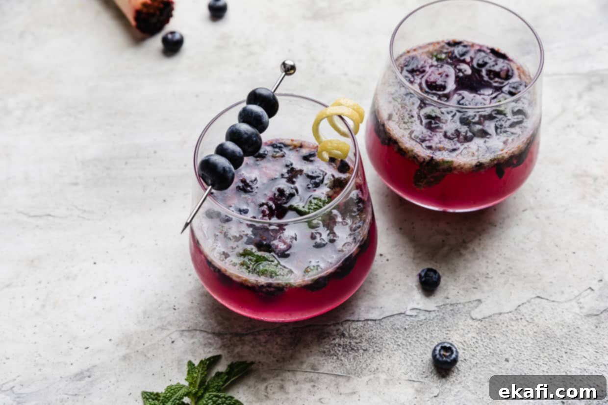 Blueberry Bliss Quencher 9 A single glass cup on a stylish gray background, filled with the vibrant blueberry mojito mocktail recipe, showcasing its inviting color and freshness.