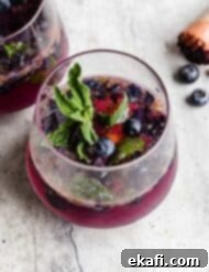 Blueberry Bliss Quencher 10 A glass cup on a gray background filled with a blueberry mojito mocktail.