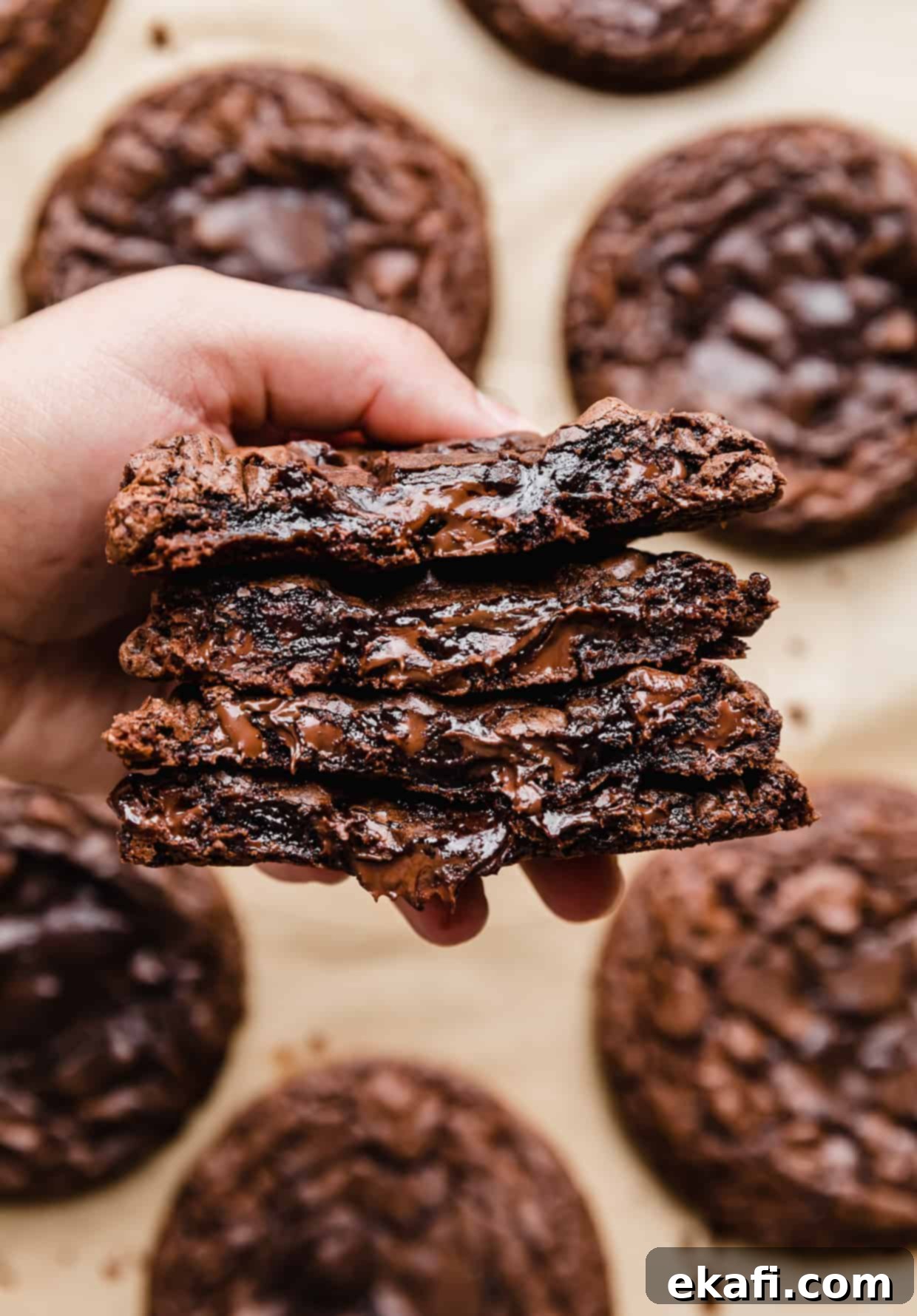 Crumbl's Signature Brownie Batter Cookies 7 A hand holding four Crumbl Brownie Batter Cookies that have been cut in half, showcasing the inner gooeyness.