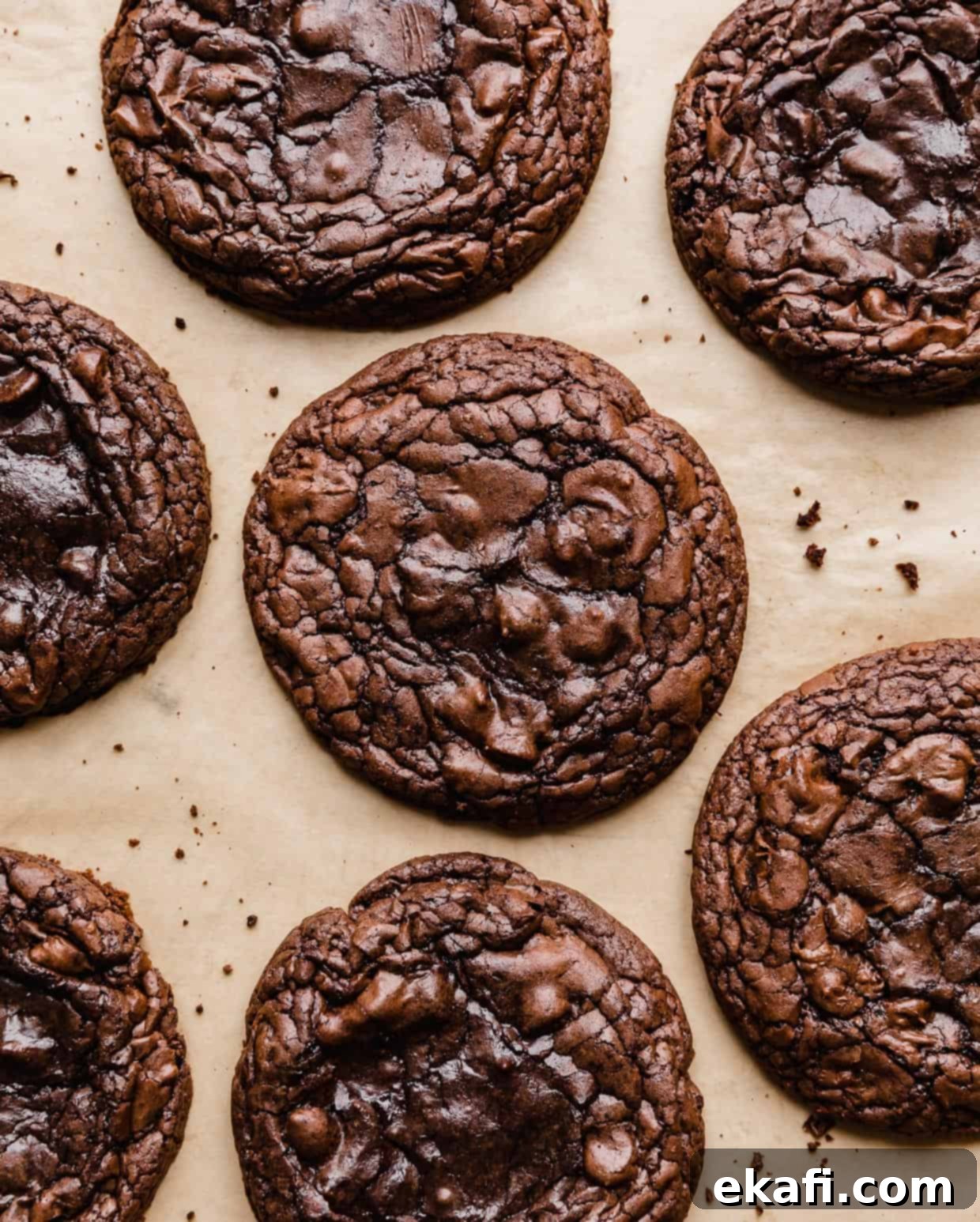 Crumbl's Signature Brownie Batter Cookies 8 Crumbl Brownie Batter Cookies with crackly tops on a tan parchment paper.