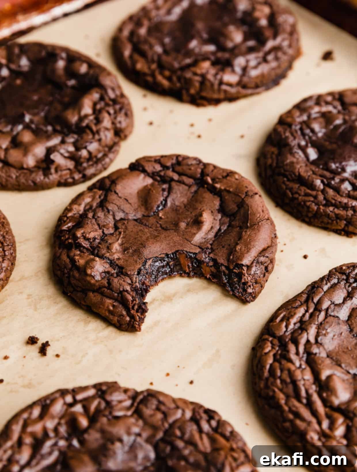 Crumbl's Signature Brownie Batter Cookies 9 A brownie batter cookie on a tan parchment paper with a bite taken out of the cookie.