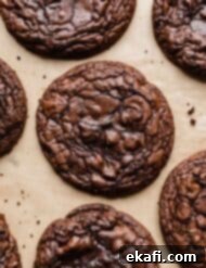Crumbl's Signature Brownie Batter Cookies 10 Crumbl Brownie Batter Cookies on a tan background with a few cookie crumbs surrounding the cookies.