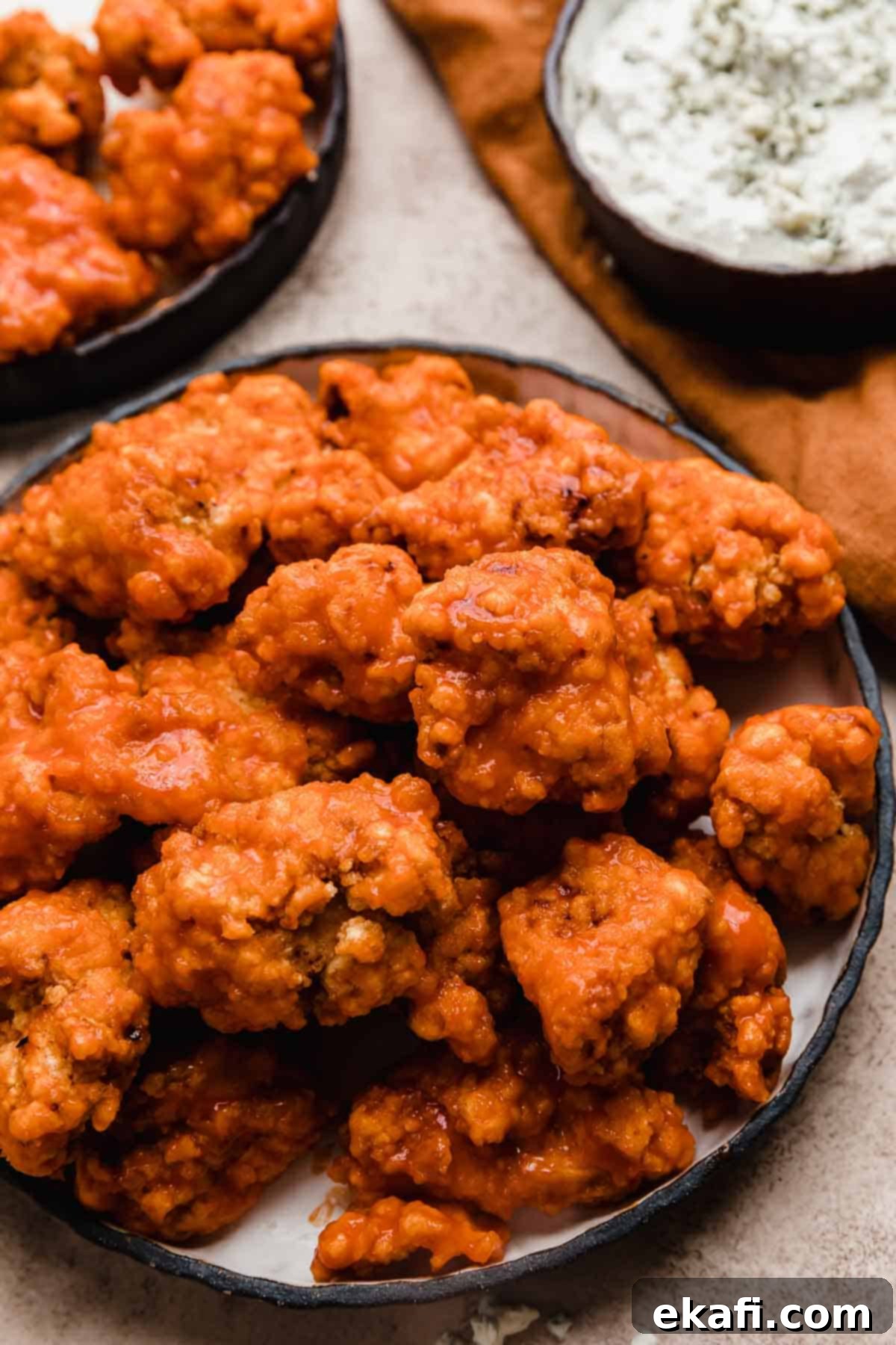 Fiery Buffalo Chicken Poppers 8 Buffalo Chicken Bites on a black rimmed plate with a blue cheese sauce in a bowl in the background, ready to be served.