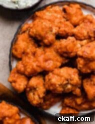 Fiery Buffalo Chicken Poppers 10 Crispy Buffalo Chicken Bites on a black plate, perfectly coated in spicy sauce.