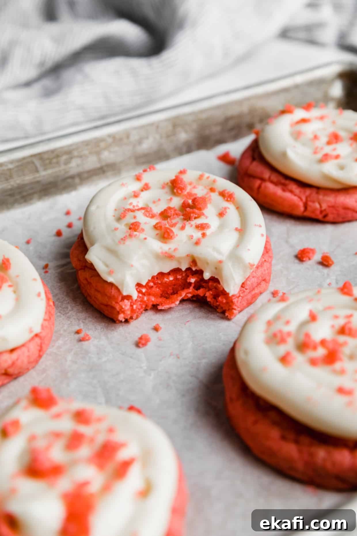 Blush Velvet Crumbl Delights 2 A Crumbl Pink Velvet Cookie topped with cream cheese frosting with a bite taken out of the cookie.