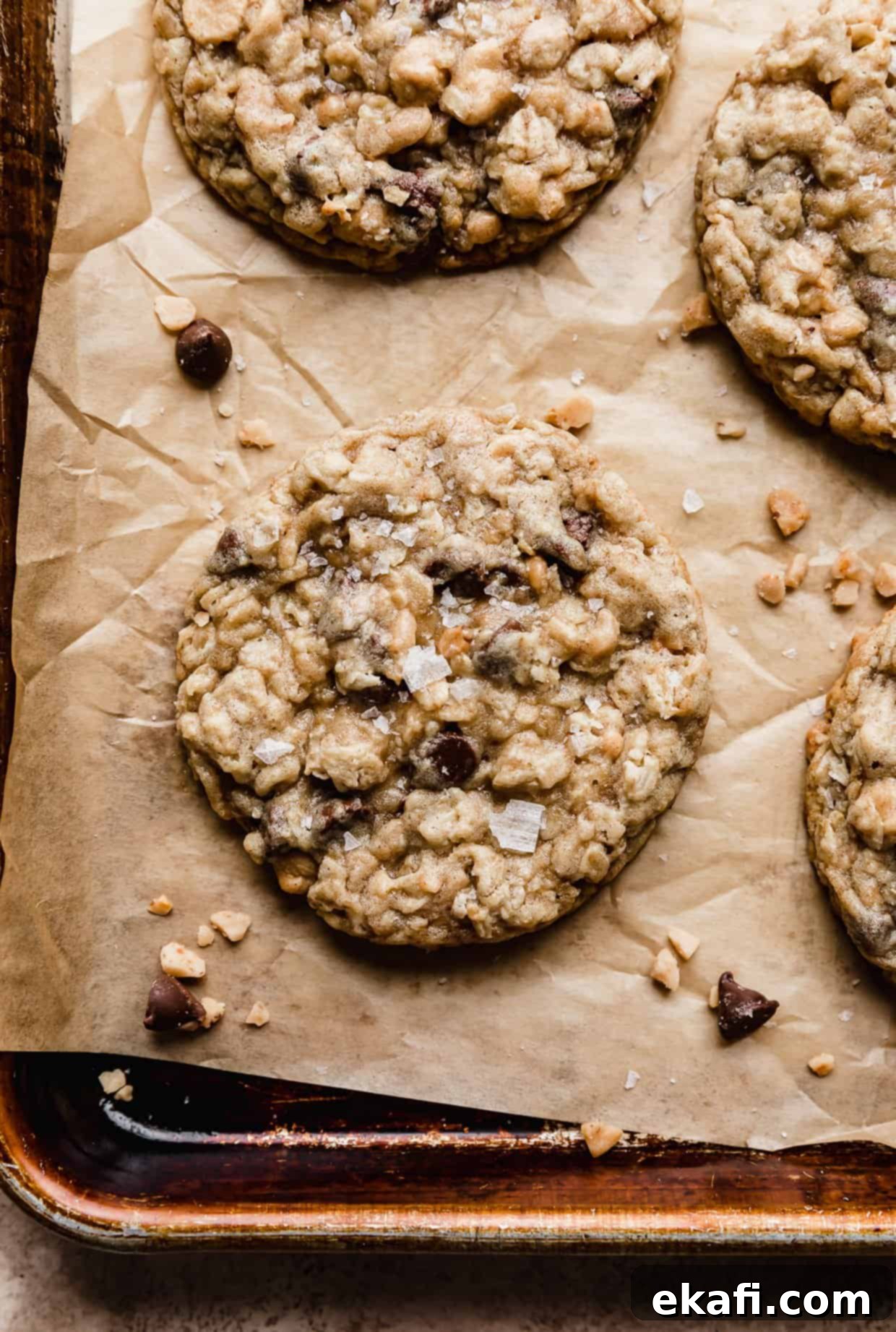 Mom's Secret Crumbl Cookie 3 A close-up of a Crumbl Mom's Recipe Cookie on a brown baking sheet, beautifully sprinkled with flaky sea salt, highlighting the texture and mixed-in chocolate chips, peanut butter chips, oats, and toffee bits.