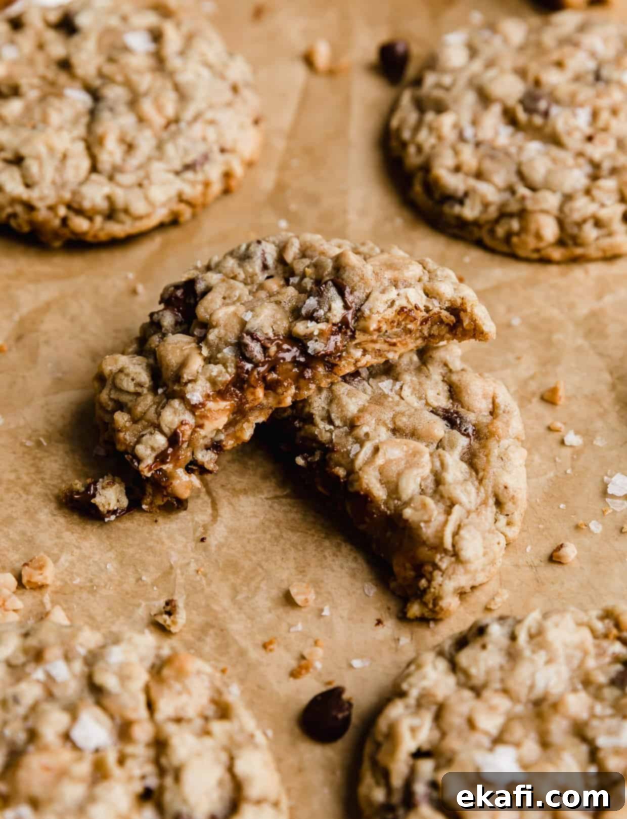 Mom's Secret Crumbl Cookie 6 A perfectly baked Crumbl Mom's Recipe oatmeal cookie, cut in half to reveal its thick, chewy interior filled with chocolate chips, peanut butter chips, and toffee, resting on tan parchment paper.