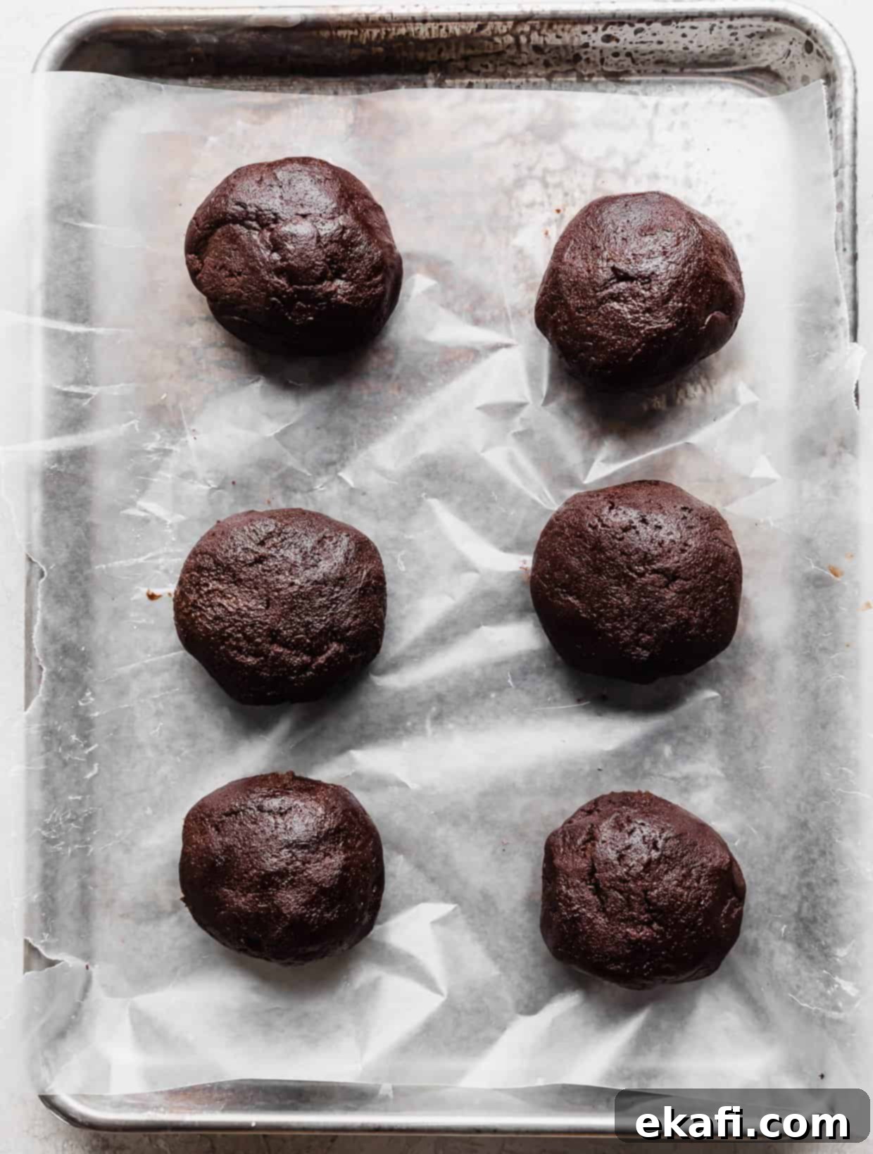 Μπισκότα με Καρδιά Λάβας 8 Έξι μπάλες ζύμης Crumbl Molten Lava Cookie σε ταψί στρωμένο με λαδόκολλα.