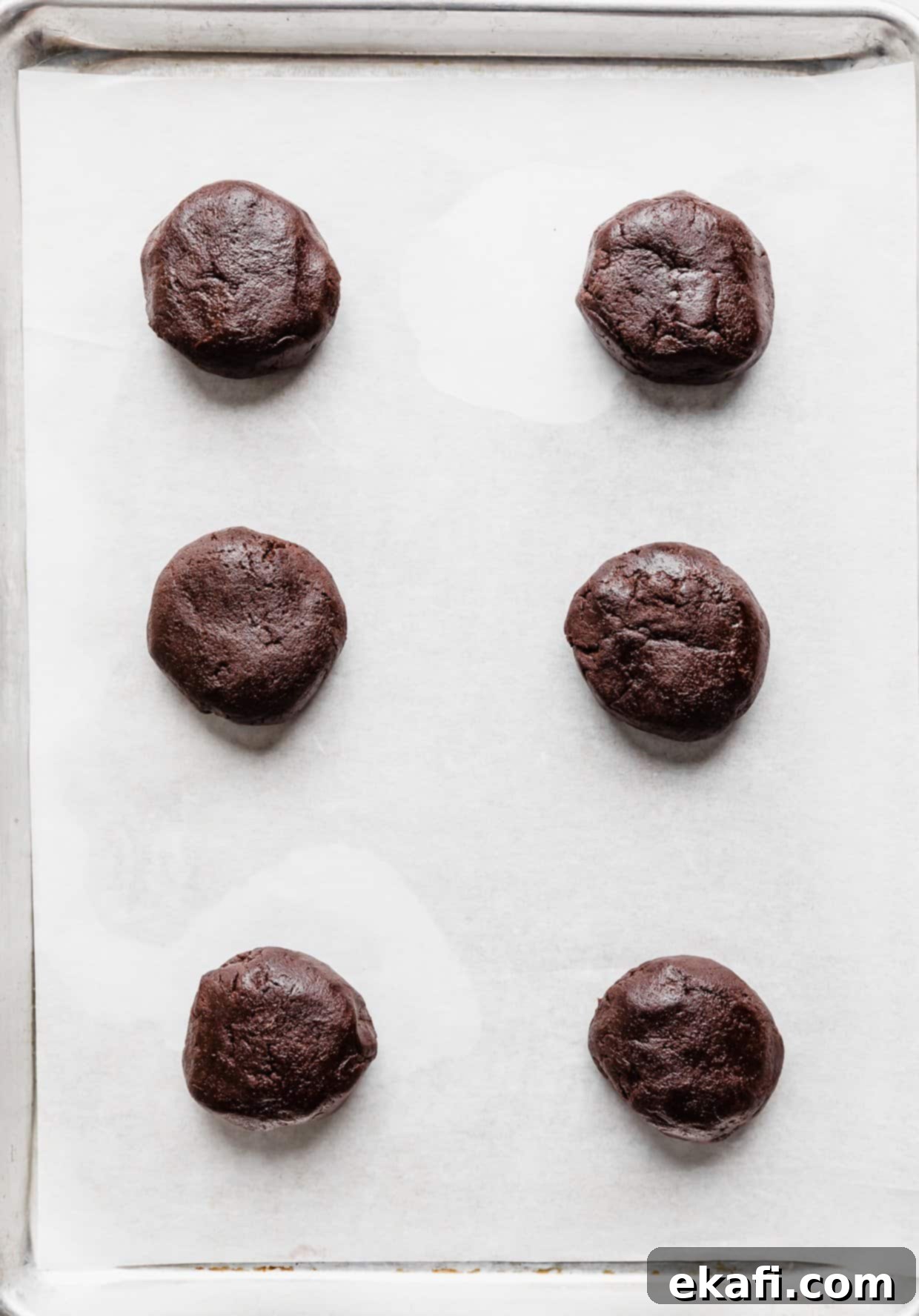 Μπισκότα με Καρδιά Λάβας 9 Έξι μπάλες ζύμης Crumbl Molten Lava Cookie σε λευκό ταψί στρωμένο με αντικολλητικό χαρτί.