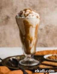 Biscoff Milkshake 8 A close-up shot of a creamy Lotus Biscoff shake in a clear glass cup, generously topped with fluffy whipped cream and a sprinkle of crushed Biscoff cookies, showcasing its rich texture and tempting appeal.