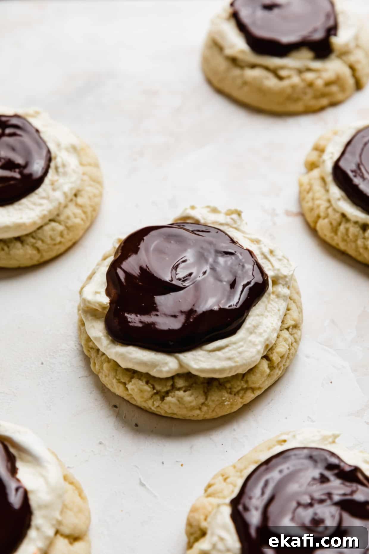 Μπισκότα Πάστα Βοστώνης 2 Crumbl Boston Cream Pie Cookies με γκανάζ σοκολάτας πάνω από τα μπισκότα που καλύπτονται με κρέμα.