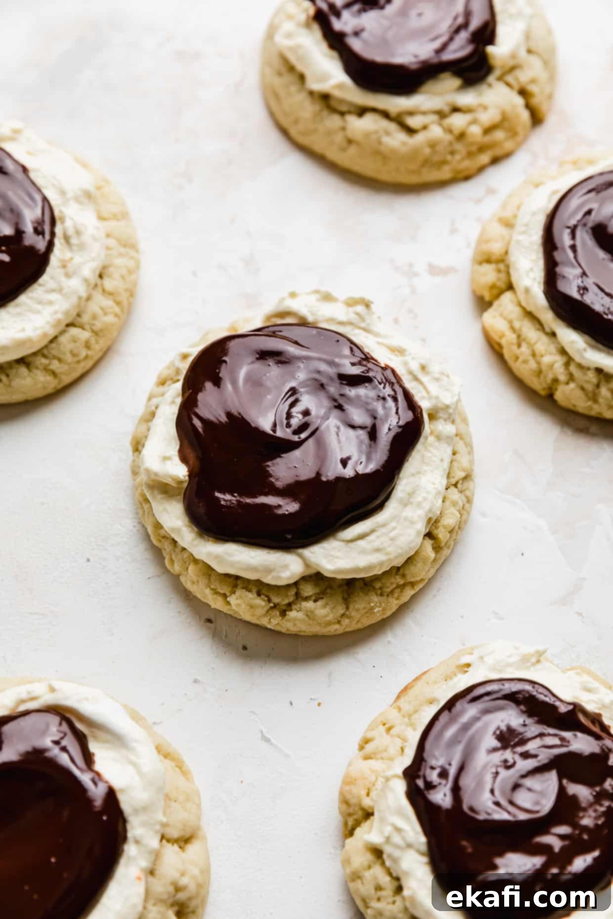 Μπισκότα Πάστα Βοστώνης 13 Crumbl Boston Cream Pie Cookies επικαλυμμένα με κρέμα ζαχαροπλαστικής και λιωμένη γκανάζ σοκολάτας, σε λευκό φόντο.