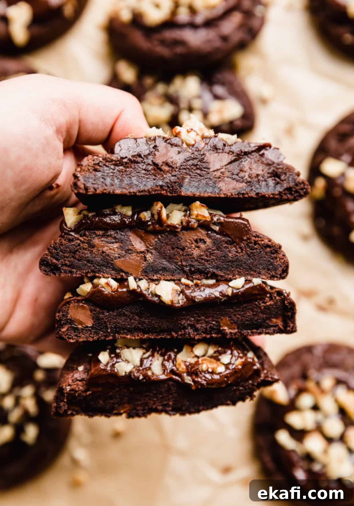 Fudgy Walnut Cookie Brownies 3 A hand holding 4 halves of Crumbl Walnut Fudge Brownie Cookies.