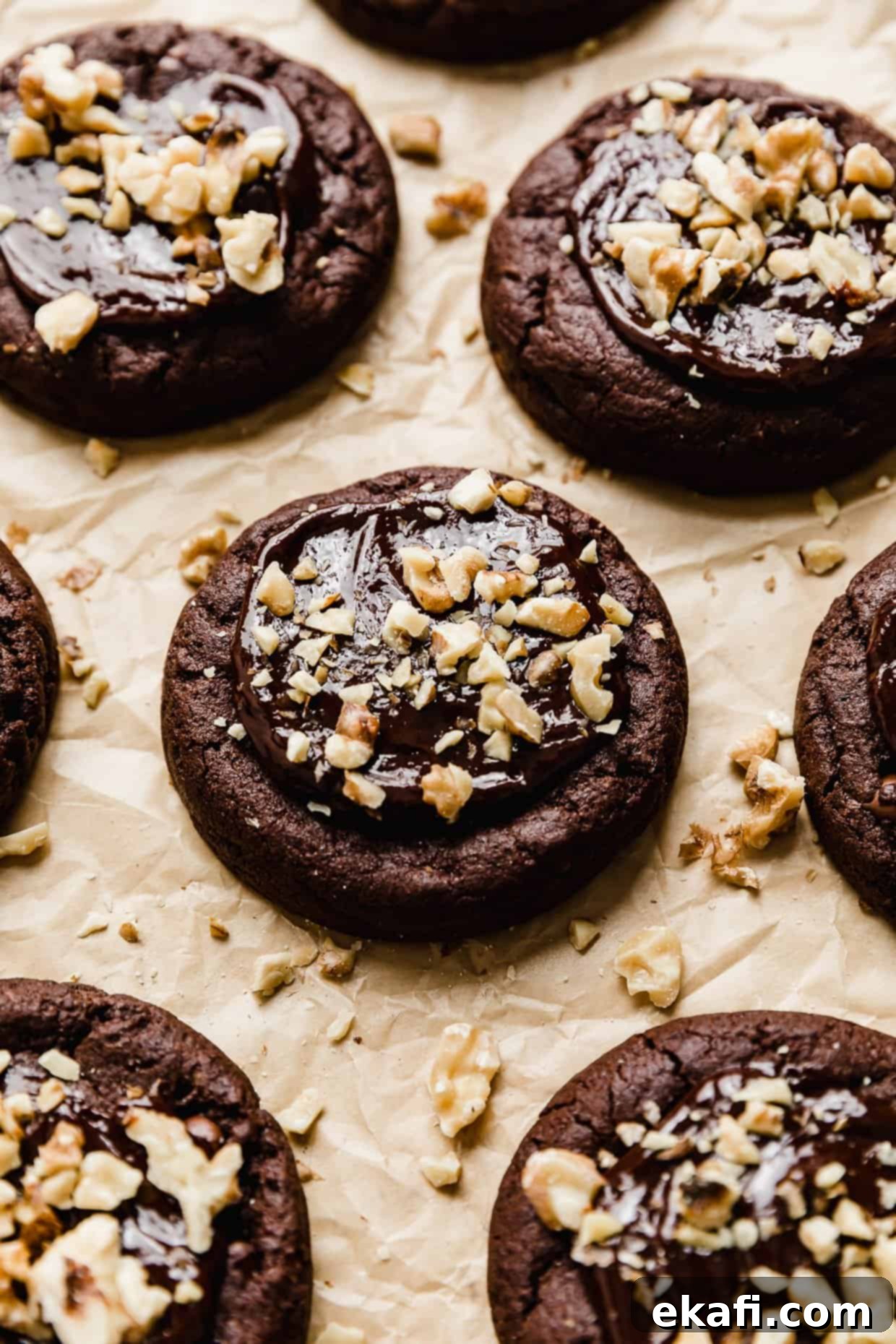 Fudgy Walnut Cookie Brownies 8 Crumbl Walnut Fudge Brownie Cookies topped with chopped walnuts on a tan parchment paper.