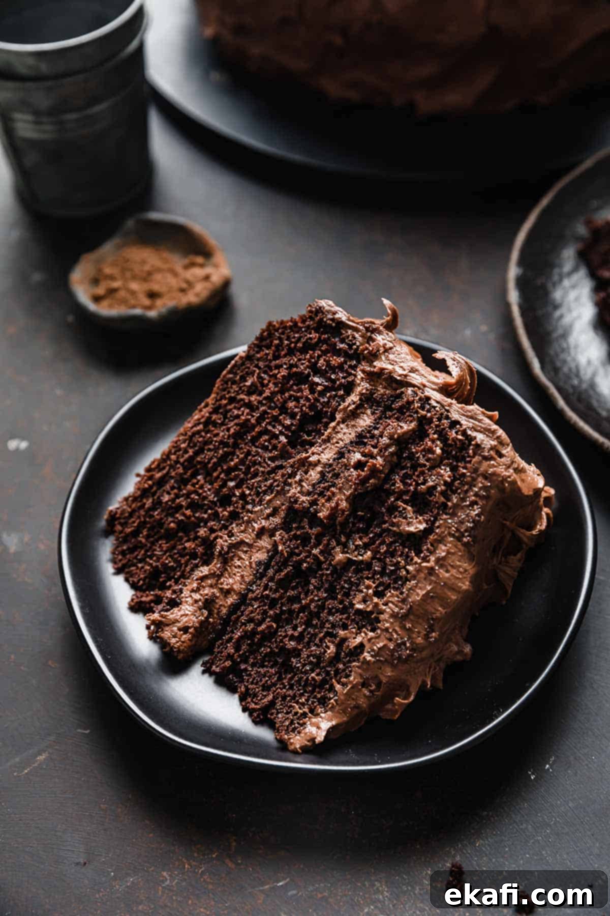 Velvet Chocolate Cream Cheese Cake 2 A slice of double layer chocolate cake on a black plate iced with chocolate cream cheese frosting.
