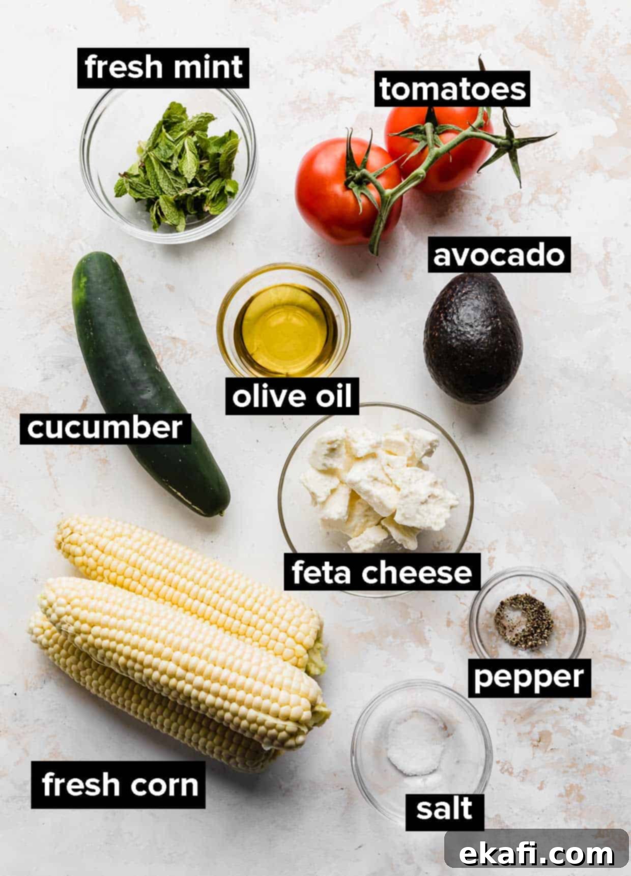 Creamy Zesty Corn Avocado Feta Salad 3 Fresh ingredients laid out on a surface, including corn cobs, tomatoes, cucumber, avocado, feta cheese, and mint, ready for feta corn salad.