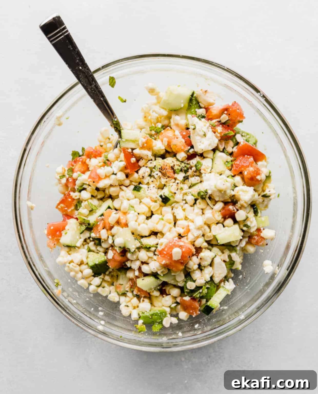 Creamy Zesty Corn Avocado Feta Salad 6 Close-up of the fully mixed Feta Corn Salad in a clear glass bowl, showcasing the vibrant colors and fresh texture of the ingredients.