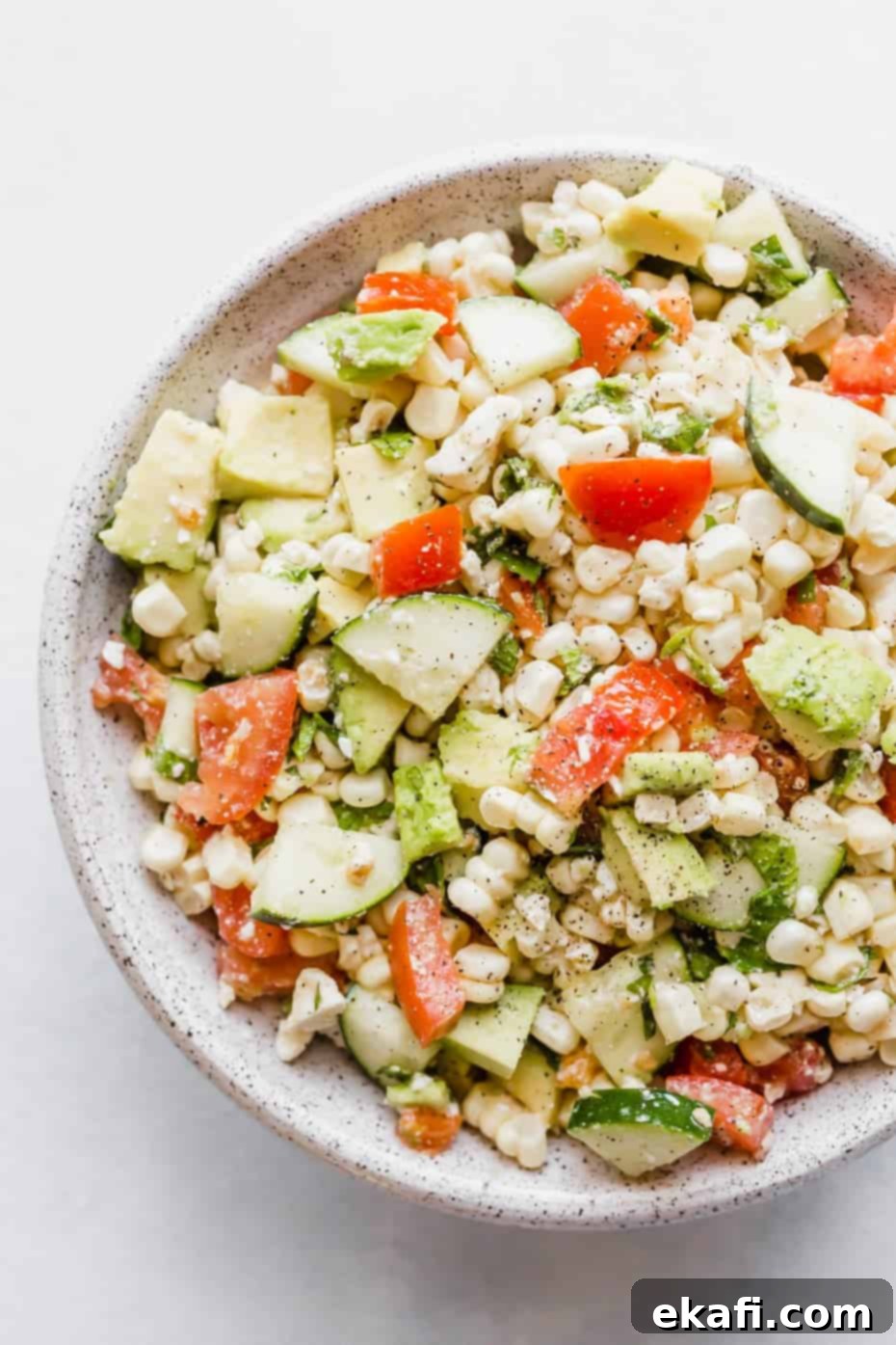 Creamy Zesty Corn Avocado Feta Salad 7 Close up image of a feta corn salad with chopped tomatoes, cucumber, corn, mint, and avocado, presented beautifully in a bowl.