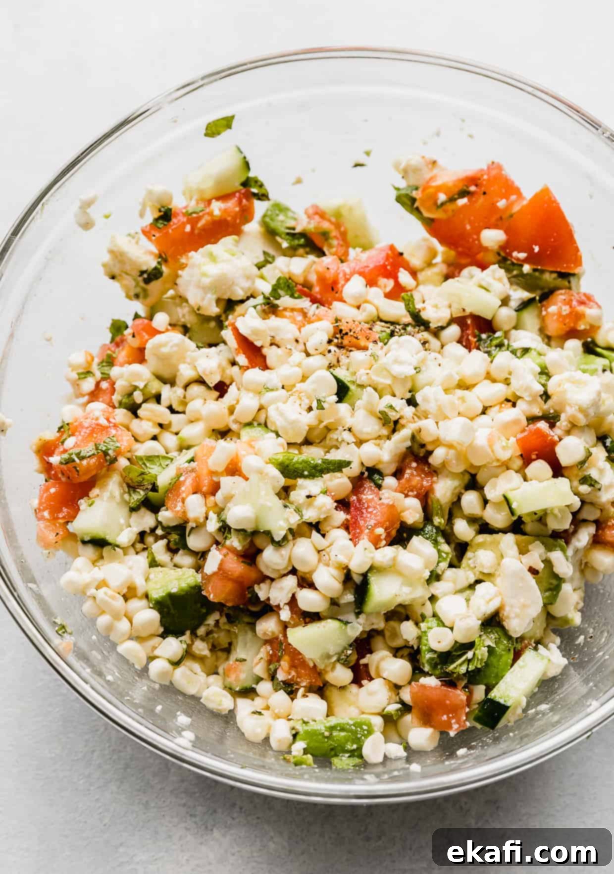 Creamy Zesty Corn Avocado Feta Salad 8 Feta Corn Salad in a clear glass bowl, artfully arranged on a white background, highlighting its fresh and vibrant appearance.