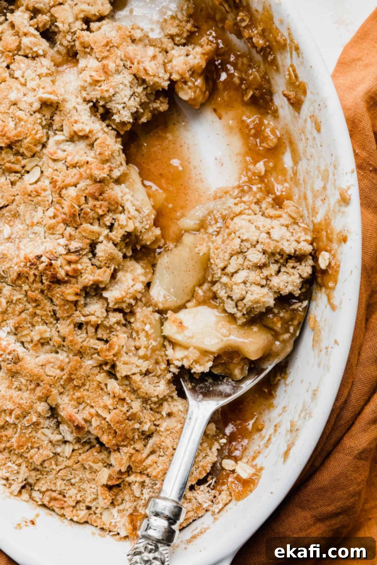 Quick & Easy Apple Crisp 15 A serving spoon scooping out homemade apple crisp from a white baking dish.