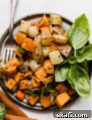 Easy Sheet Pan Root Roast 8 A gray plate on a white background with easy Sheet Pan Roasted Root Vegetables topped with herbs on it.