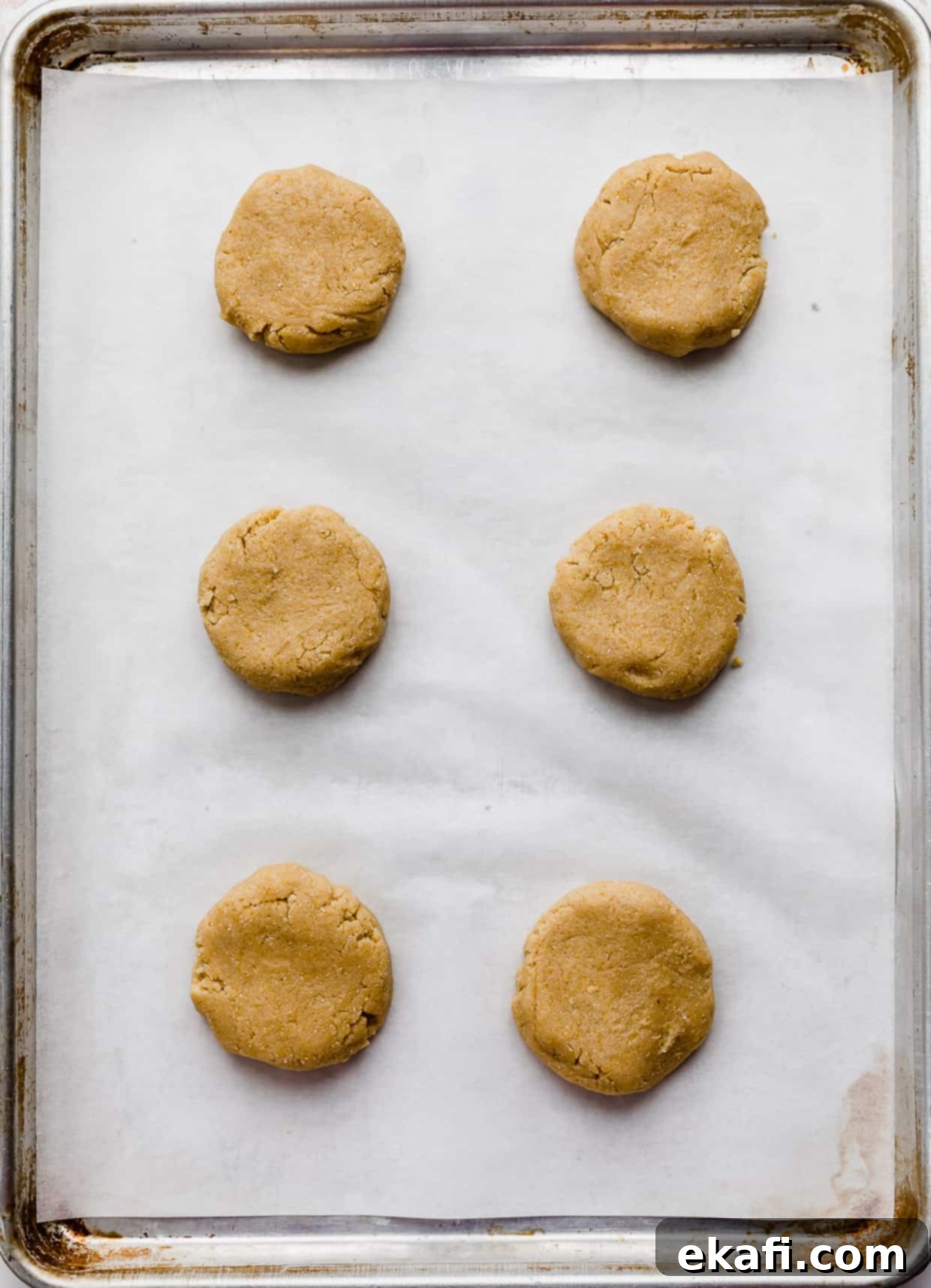 Crumbl Καλαμποκένιο Μπισκότο 5 Μπάλες ζύμης cornbread crumbl cookie σε λευκό ταψί με αντικολλητικό χαρτί, έτοιμες για ψήσιμο.