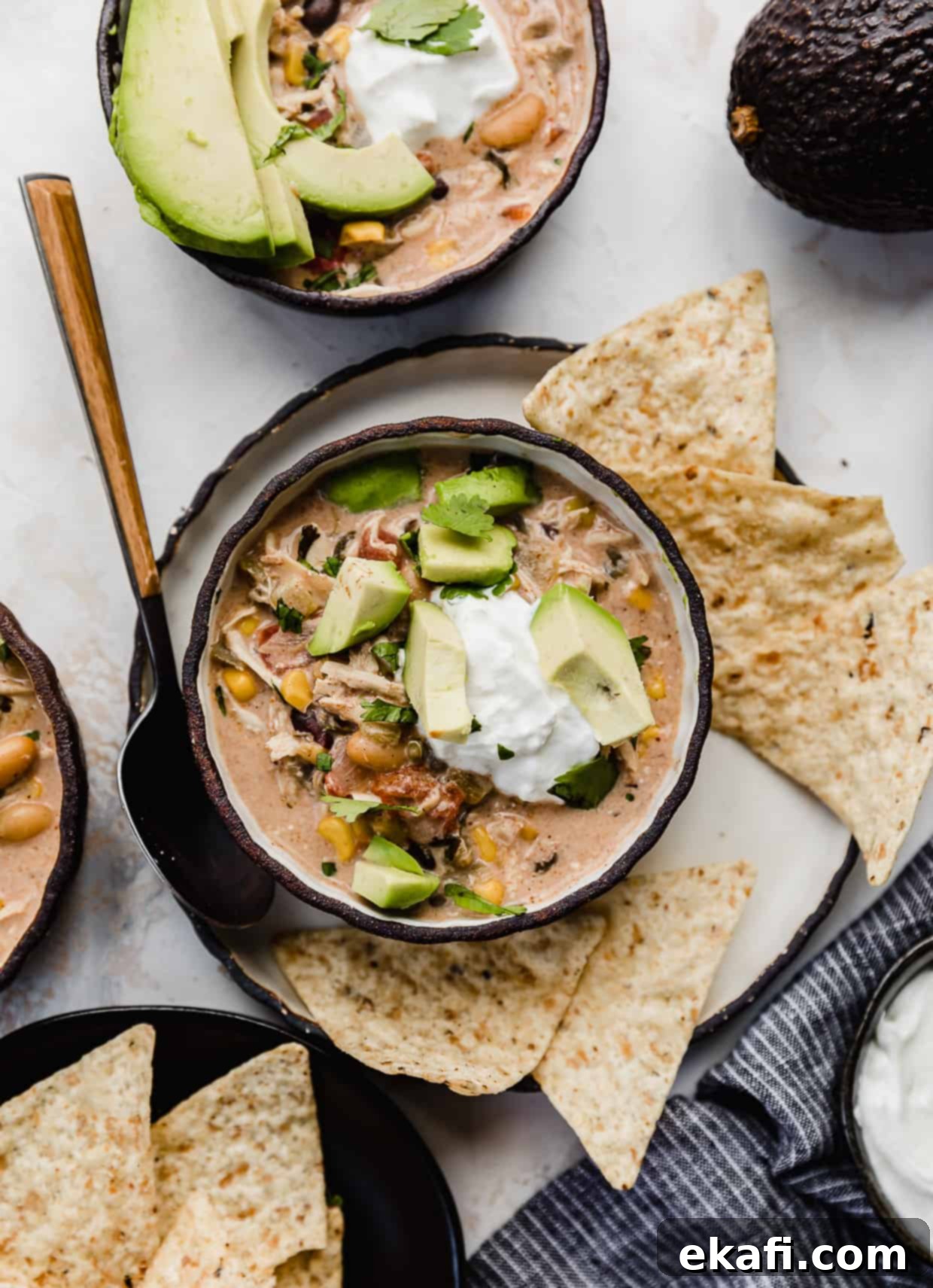 Dreamy Cream Cheese Chicken Chili 2 A black bowl filled with Crock Pot Cream Cheese Chicken Chili that's been topped with sour cream, avocado, and fresh cilantro.