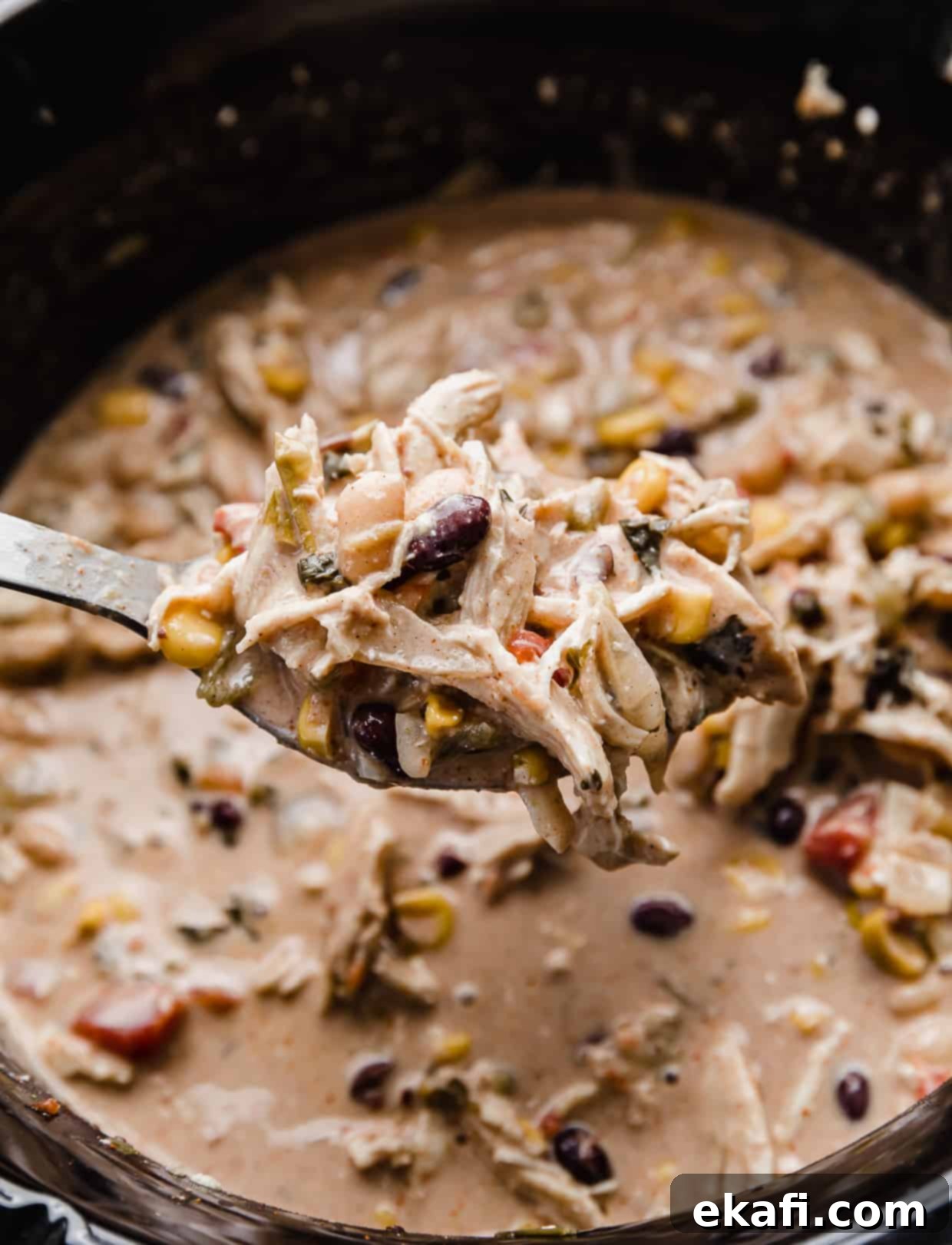 Dreamy Cream Cheese Chicken Chili 6 A metal spoon filled with creamy chicken chili, showing black beans and corn.