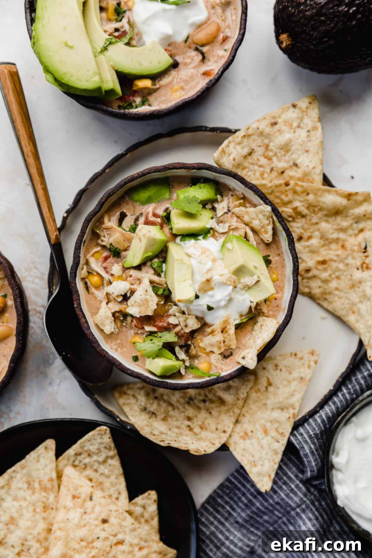 Dreamy Cream Cheese Chicken Chili 7 Crock Pot Cream Cheese Chicken Chili in a black bowl with tortilla chips, avocado, and sour cream on top, ready to be enjoyed.