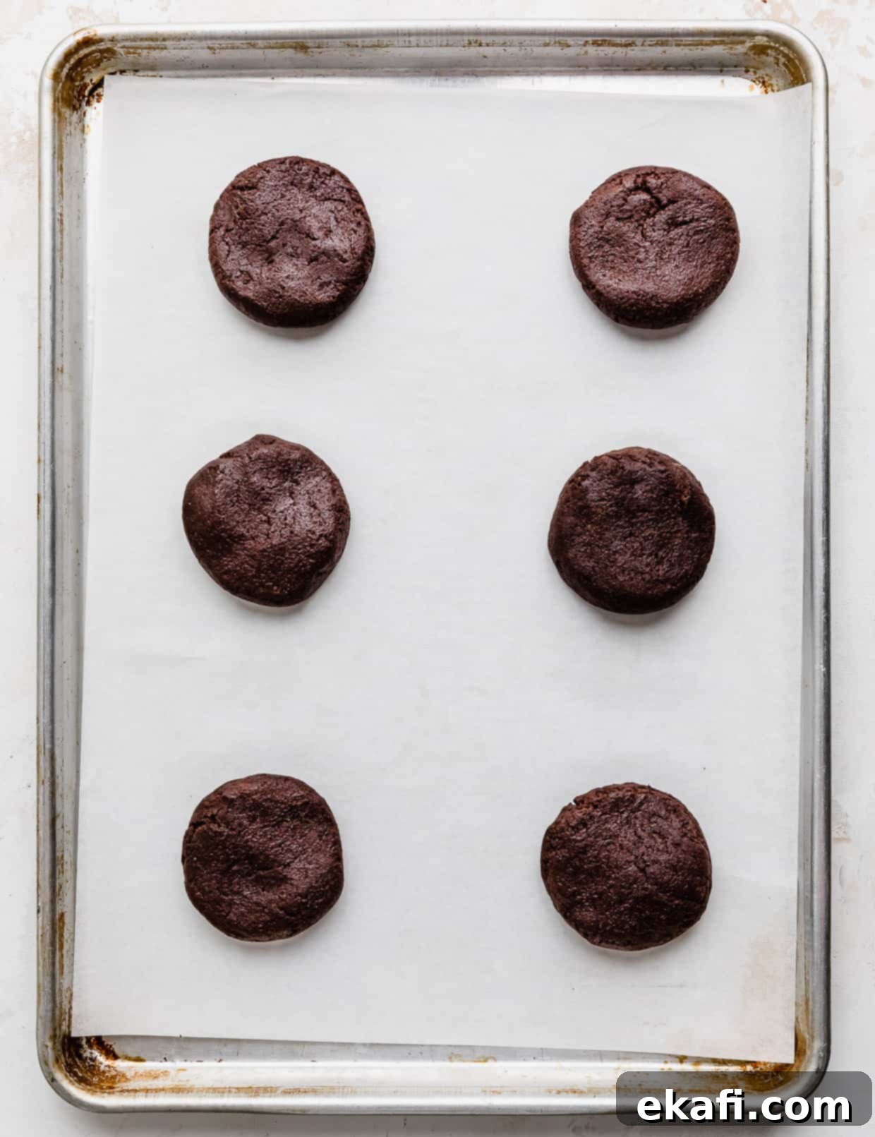 Hostess Cupcake Cookies 4 Six perfectly portioned chocolate cookie dough balls, gently pressed into thick disks, resting on a white parchment paper lined baking sheet, ready for the oven.