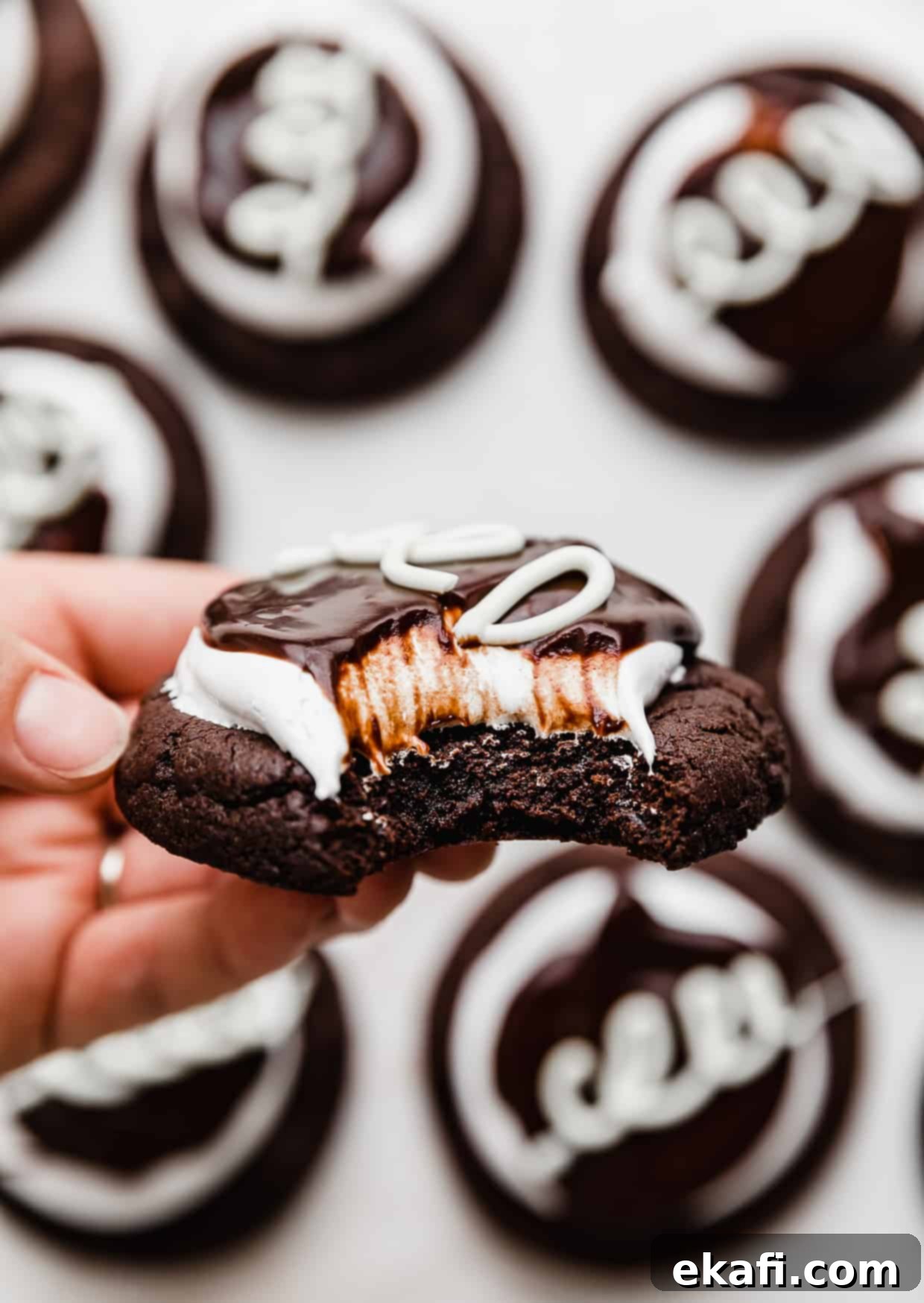 Hostess Cupcake Cookies 9 A hand holding a beautifully crafted Hostess Cupcake Cookie with a bite taken out, revealing the soft chocolate cookie, airy marshmallow frosting, and glossy ganache.