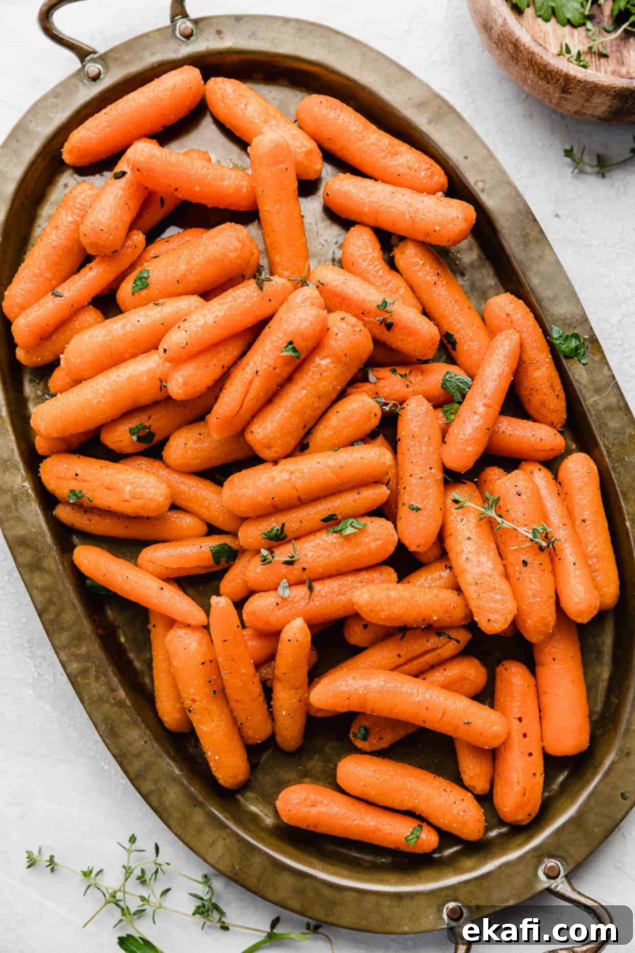 Caramelized Baby Carrots 2 Roasted Baby Carrots topped with thyme and parsley on a bronze oval plate.