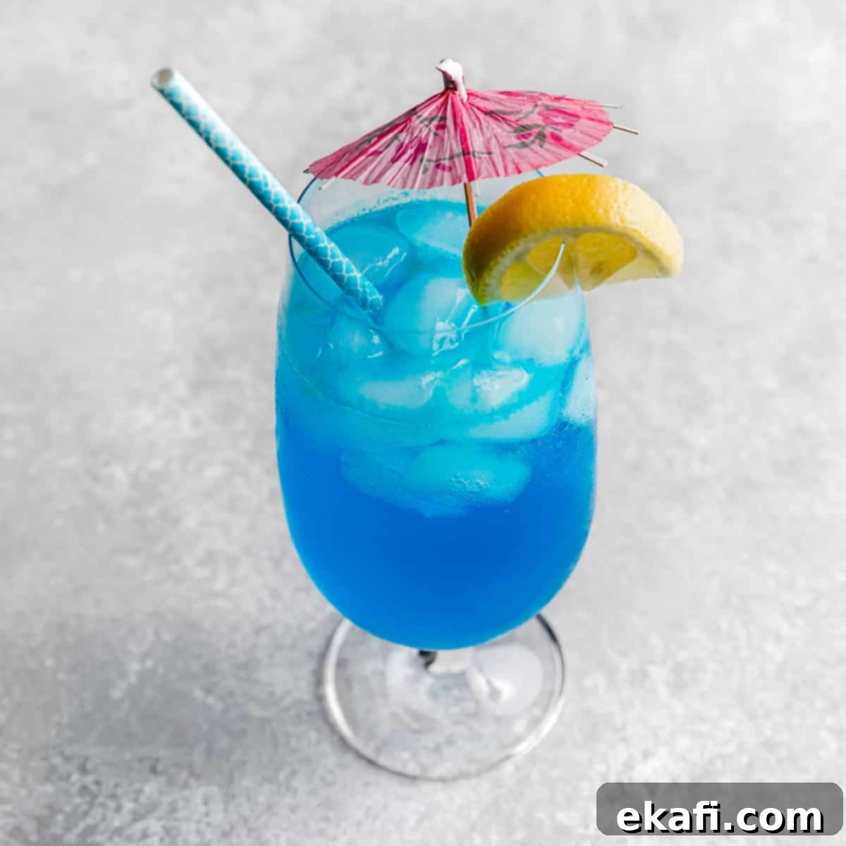 Δροσερά Μοκτέιλ με Sprite 5 Ένα Blue Lagoon Mocktail σε ένα μεγάλο γυάλινο ποτήρι με μια ροζ ομπρέλα και φέτα λεμονιού στο χείλος.
