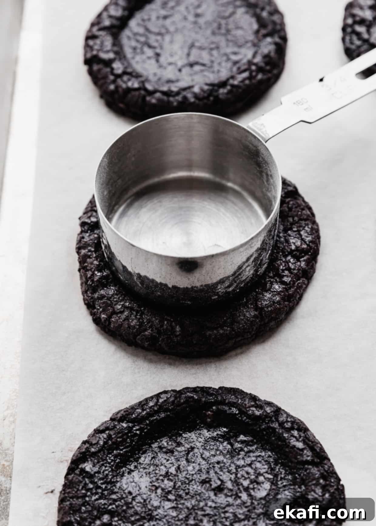Decadent French Silk Pie Cookies 5 A metal measuring cup pressing into the top of an homemade Oreo cookie, for making a French Silk Pie Cookie.