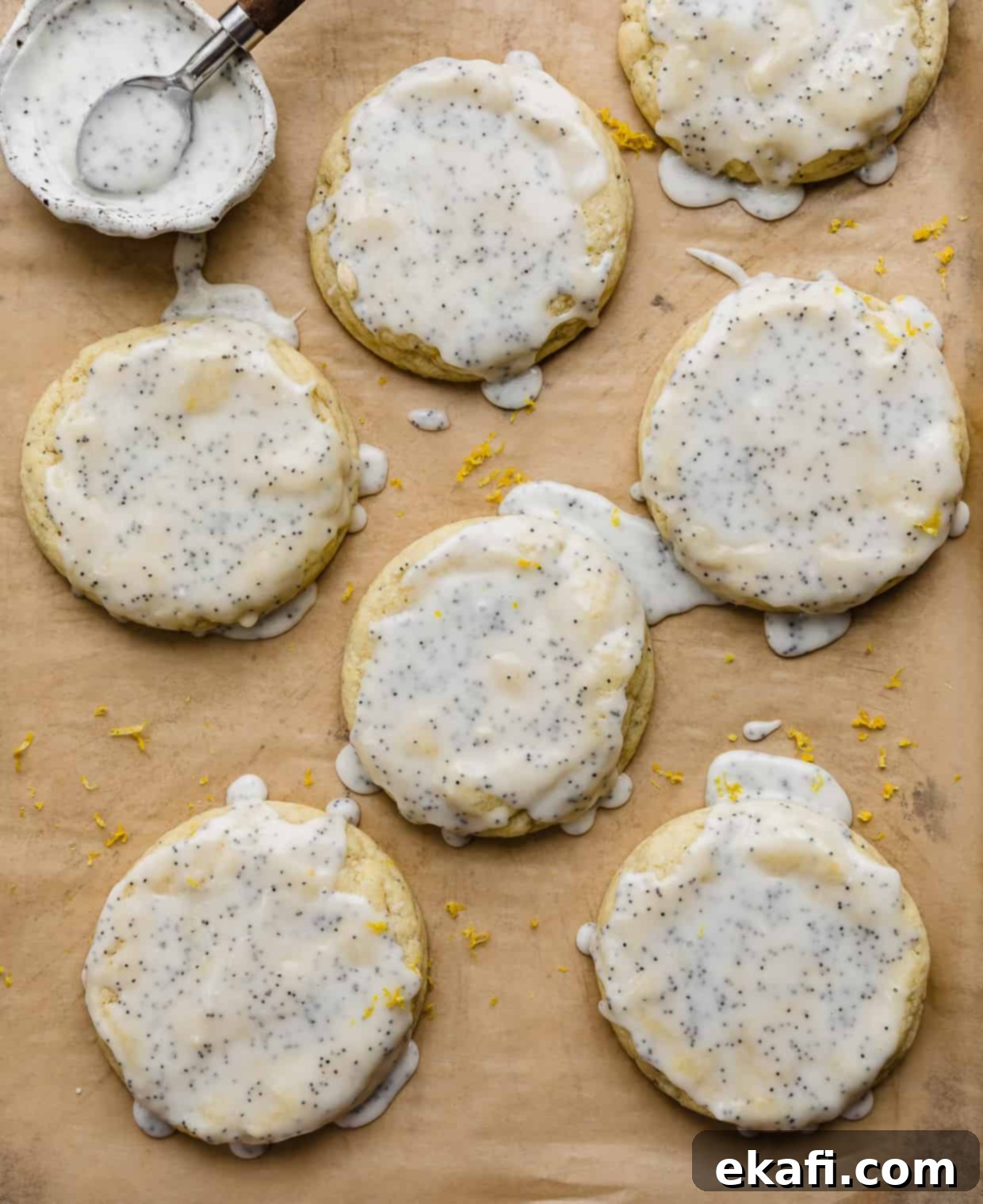 Zesty Lemon Poppy Seed Delights 12 A lemon almond poppy seed glaze overtop of lemon poppy seed cookies that are on a tan colored parchment paper.