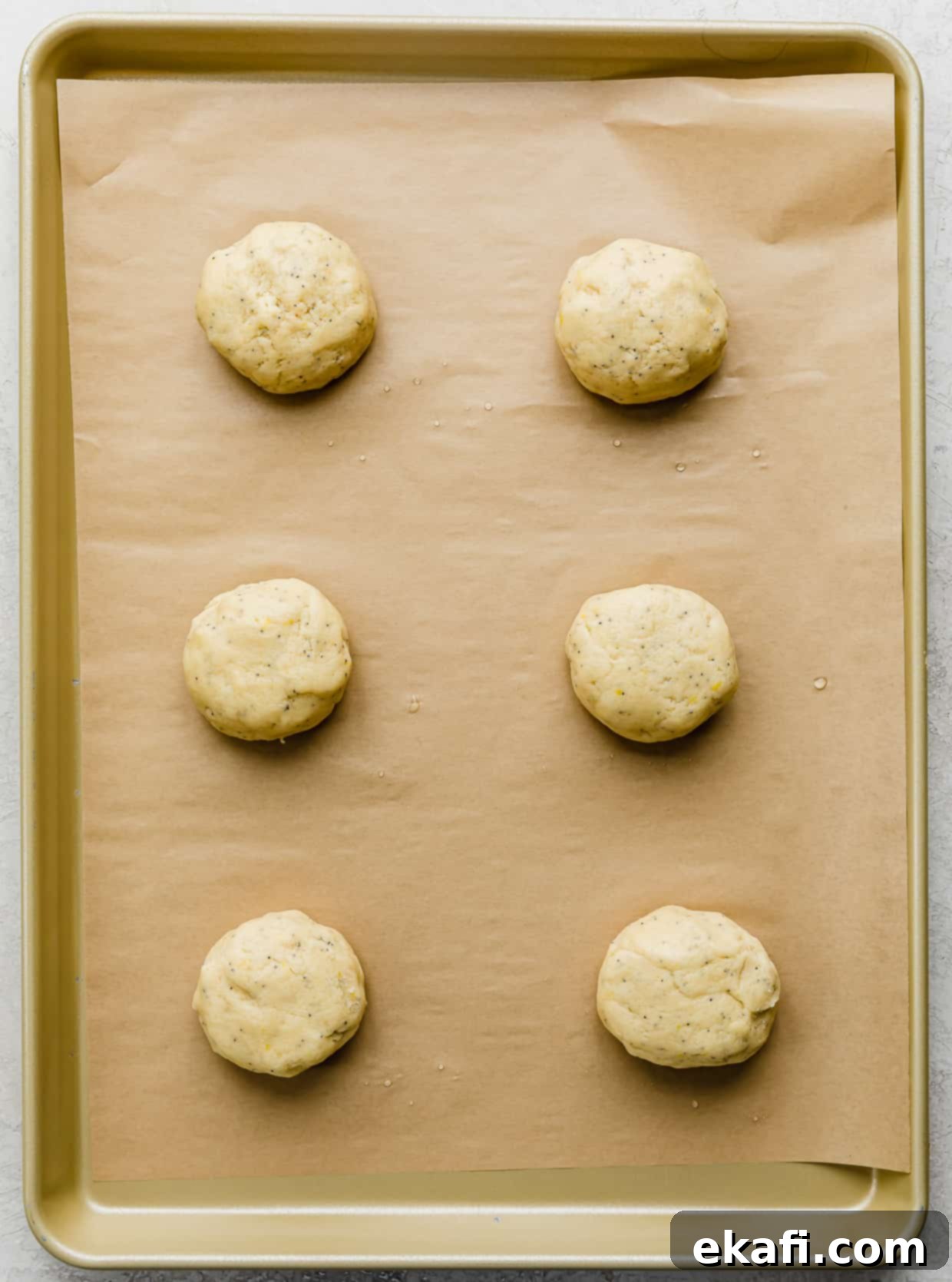 Zesty Lemon Poppy Seed Delights 9 Lemon Poppy Seed Cookie dough balls on a tan parchment lined baking sheet, prior to baking.