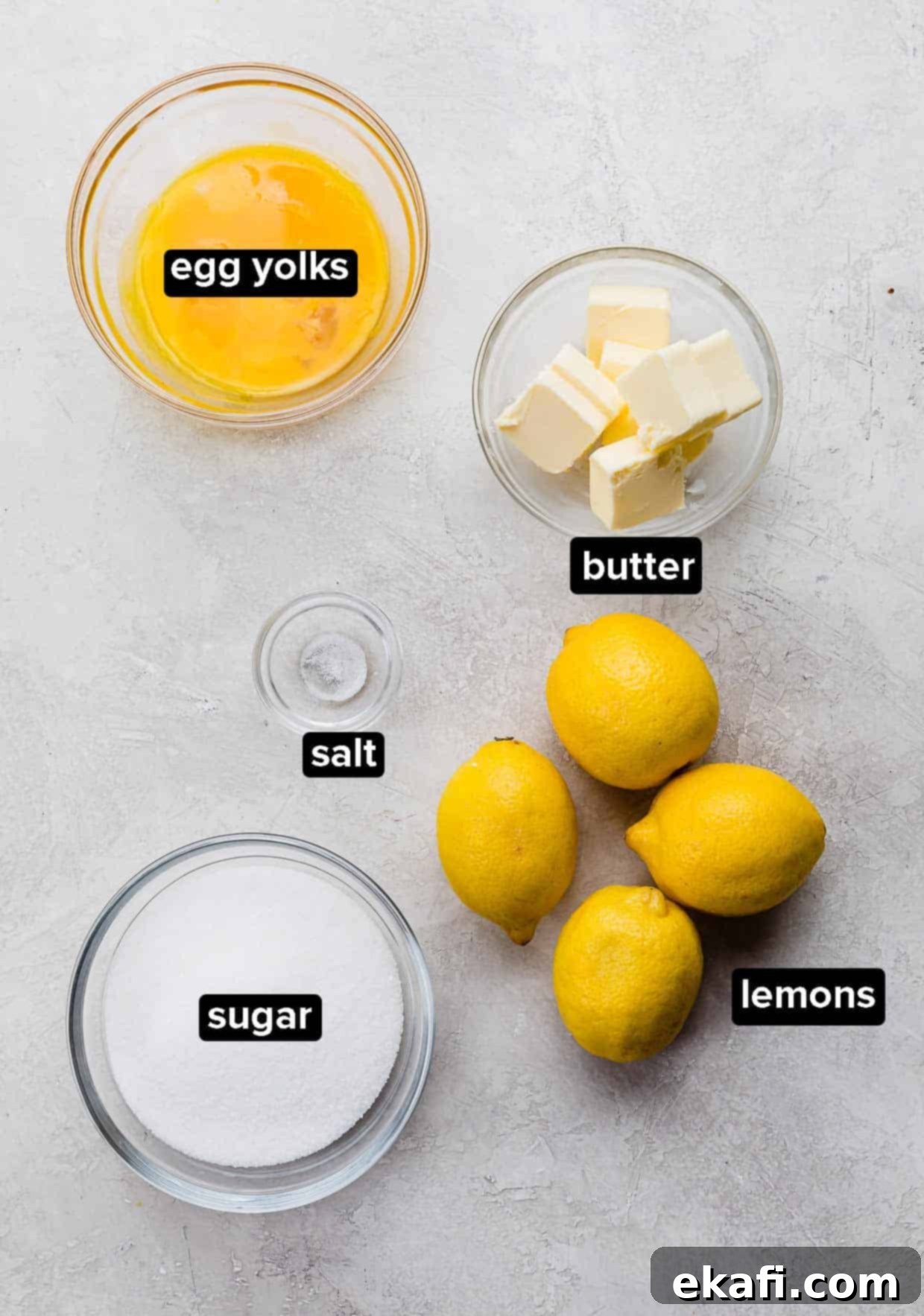 Luscious Lemon Curd Perfection 3 Homemade lemon curd ingredients portioned into glass bowls, on a gray background: sugar, lemons, salt, egg yolks, and butter.