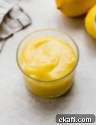 Luscious Lemon Curd Perfection 8 Homemade Lemon Curd in a glass cup on a light gray background with a lemon half in the background.