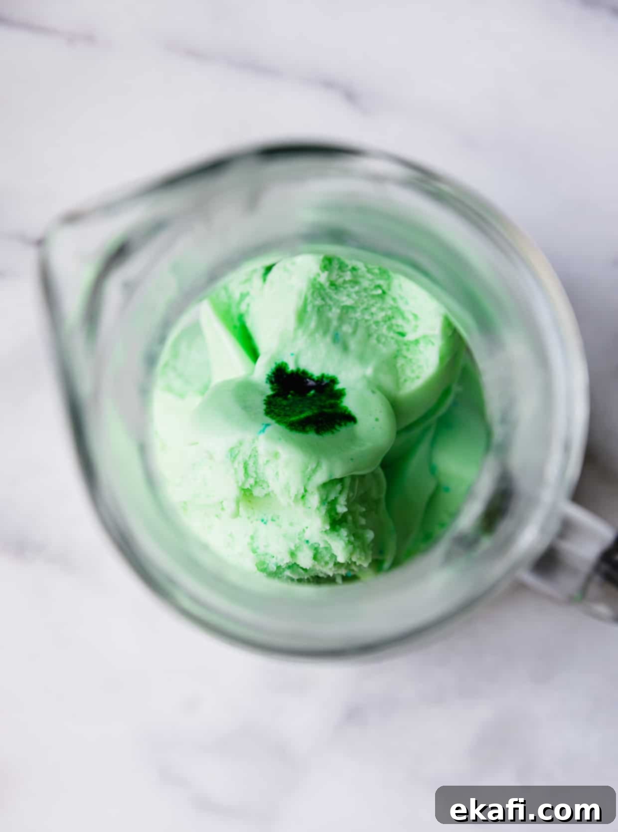 Shape-Shifter's Brew 4 An overhead shot of a clear glass pitcher showing creamy lime sherbet with a drop of green food coloring, ready to be mixed into a Polyjuice Potion.