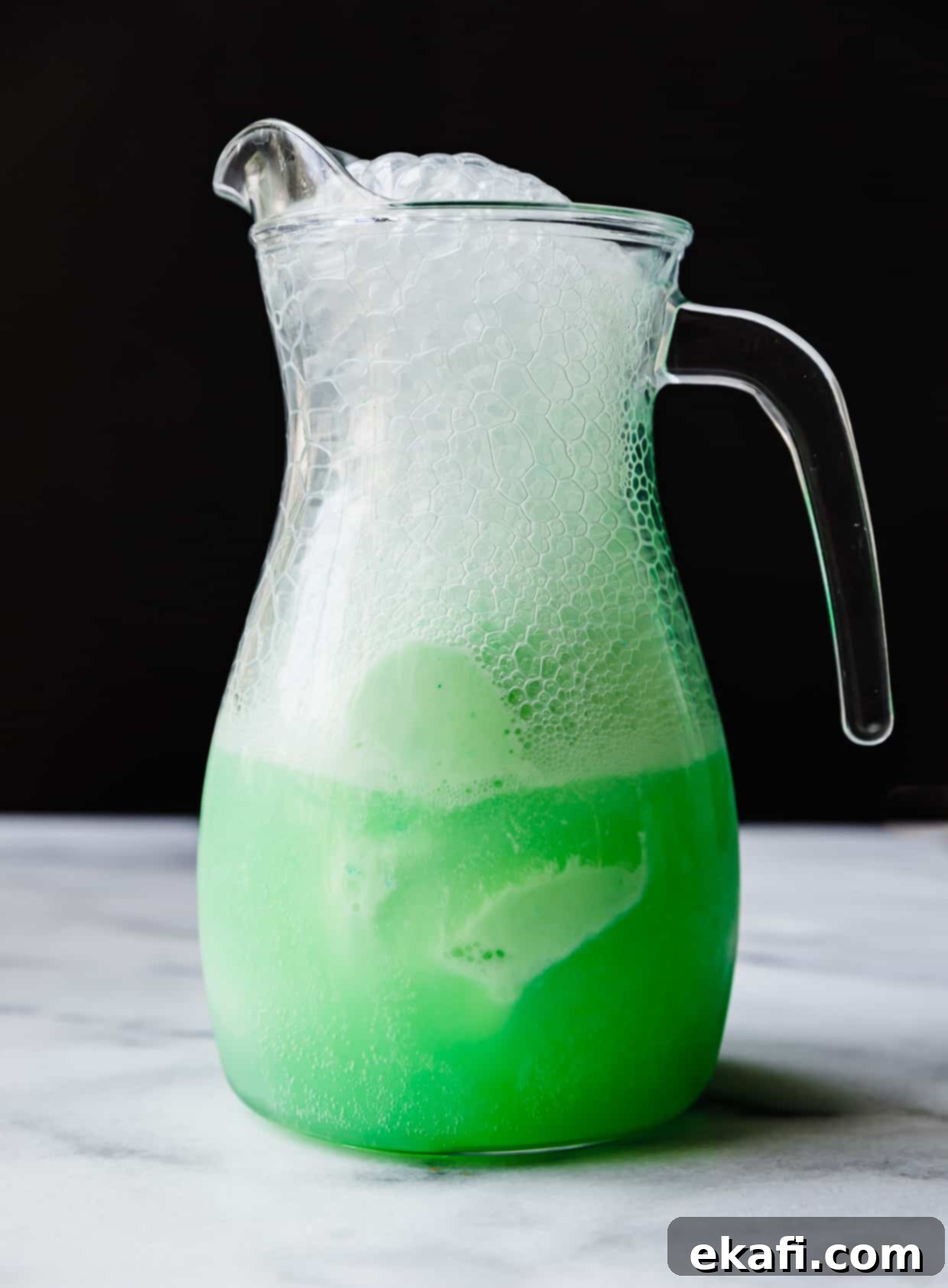 Shape-Shifter's Brew 5 A clear glass pitcher brimming with a frothy, vibrant green Polyjuice Potion, ready to serve at a themed party.